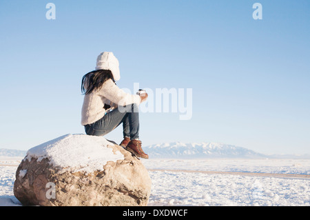 Woman sitting on rock with cup in winter, Colorado, USA Stock Photo