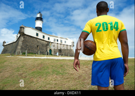 Brazilian football player standing with vintage brown soccer ball at Farol da Barra lighthouse in Salvador Stock Photo