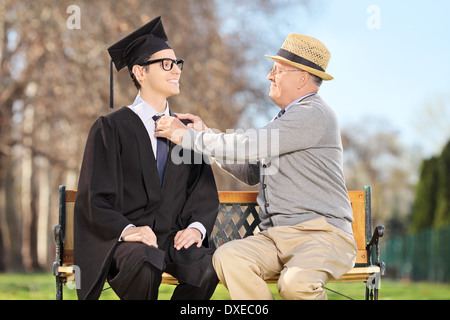 Father preparing his son for graduation seated on wooden bench in park Stock Photo