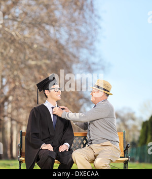 Graduate student and his proud father sitting on a wooden bench in park Stock Photo
