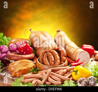 Still-life with sausage products, vegetables and herbs on a yellow-brown background. Stock Photo
