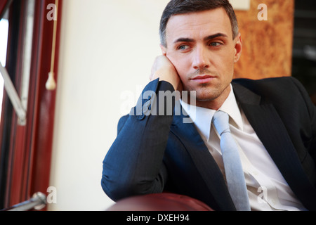 Pensive businessman sitting and looking in window at office Stock Photo