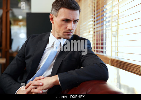 Pensive businessman sitting and looking in window at office Stock Photo