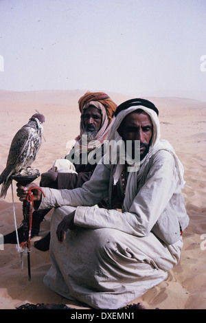 Two Arab men, one holding a falcon, in the desert in Abu Dhabi in 1964 Stock Photo