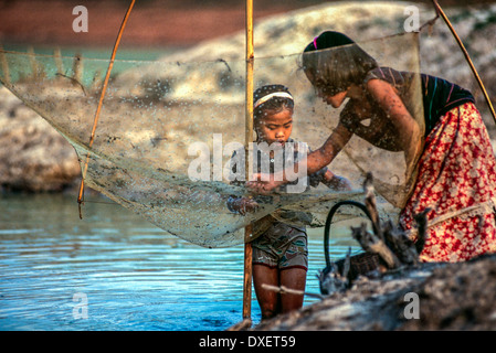 Laos children mending fishing net bamboo poles riverbank trees