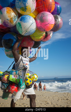RIO DE JANEIRO, BRAZIL - JANUARY 19, 2014: Beach vendor selling colorful beach balls carries his merchandise along Ipanema Beach Stock Photo