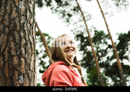 Portrait of girl standing next to tree in park, looking upward, Germany Stock Photo