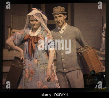 This vintage photograph shows a man and woman carrying suitcases, possibly embarking on a journey or travel. The image reflects travel customs and the lifestyle of the early 20th century, capturing the clothing and attitudes of the time. Stock Photo