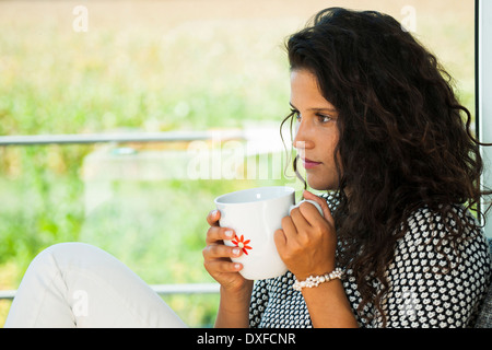 Teenage girl sitting next to window, holding cup in hands, Germany Stock Photo