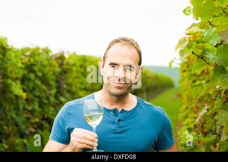 Portrait of vintner holding glass of wine in vineyard, smiling and looking at camera, Rhineland-Palatinate, Germany Stock Photo