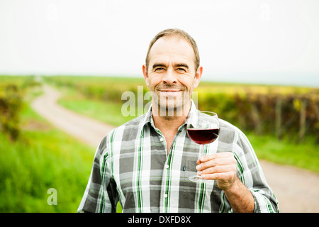 Portrait of vintner standing in vineyard, holding glass of wine, smiling and looking at camera, Rhineland-Palatinate, Germany Stock Photo