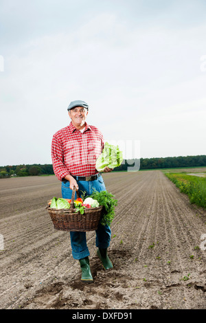 Farmer standing in field with basket of fresh vegetables, smiling and looking at camera, Hesse, Germany