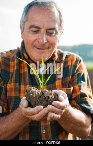 Close-up portrait of farmer standing in field, holding seedling plant from crop, Germany Stock Photo