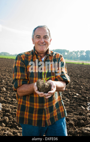 Portrait of farmer standing in field, holding seedling plant from crop, Germany Stock Photo