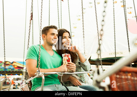 Young couple sitting on amusement park ride eating popcorn, Germany Stock Photo