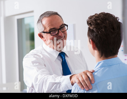 Businessman with hand on shoulder of apprentice in office, Germany Stock Photo