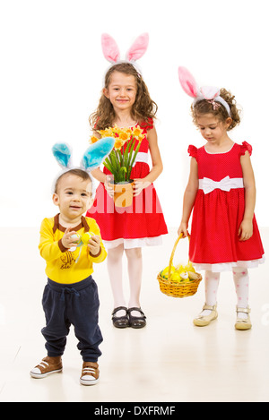 Happy toddler boy in front of camera and his sisters in background wearing all bunny ears and holding Easter basket Stock Photo