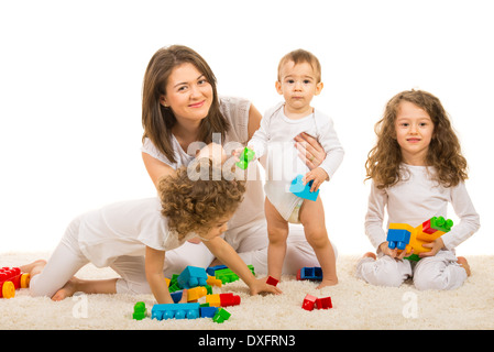 Cheerful family of mother and three kids sitting on carpet with toys Stock Photo