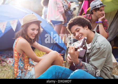 Man playing guitar outside tents at music festival Stock Photo