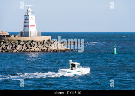 A small white boat passes a lighthouse as it heads out to sea past the Pilot Pier in Hartlepool, north east England. Stock Photo