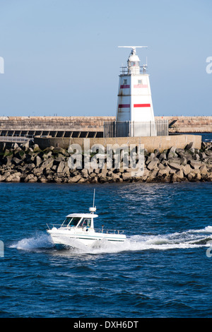 A small white boat passes a lighthouse as it returns from the sea past the Pilot Pier in Hartlepool, north east England. Stock Photo