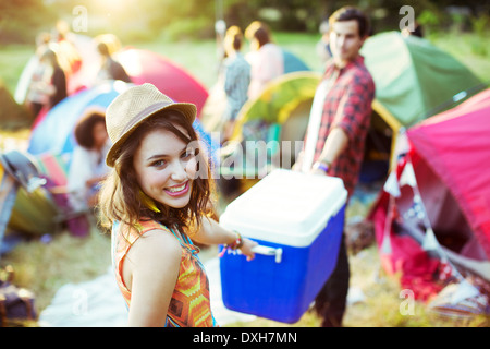 Portrait of woman helping man carry cooler outside tents at music festival Stock Photo