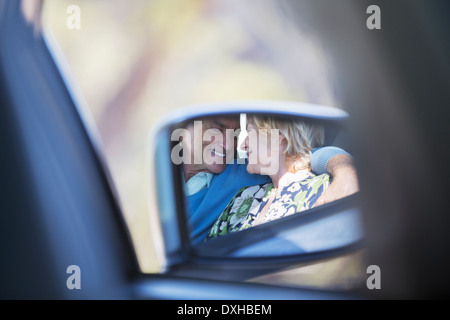 Side-view mirror reflection of couple hugging inside car Stock Photo