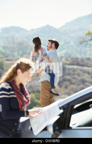 Father holding daughter at roadside while woman checks map Stock Photo