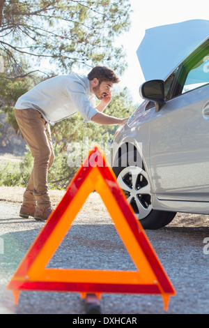 Man at roadside checking car engine behind warning triangle Stock Photo