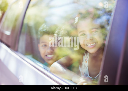 Portrait of happy brother and sister looking out car window Stock Photo