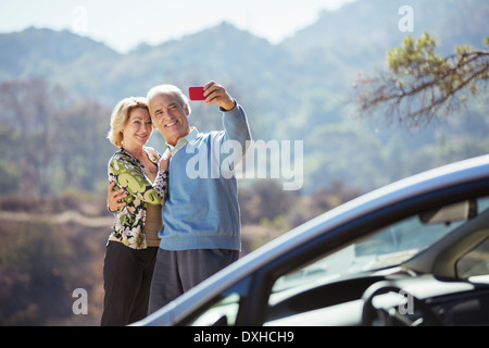 Senior couple taking self-portrait with cell phone outside car Stock Photo