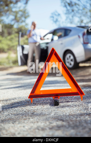 Man talking on cell phone at roadside behind warning triangle Stock Photo