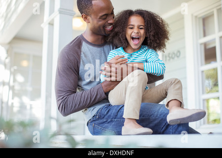 Father tickling daughter on porch Stock Photo