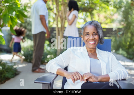 Portrait of smiling senior woman on patio with family in background Stock Photo