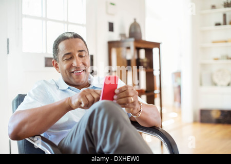 Senior man text messaging with cell phone in living room