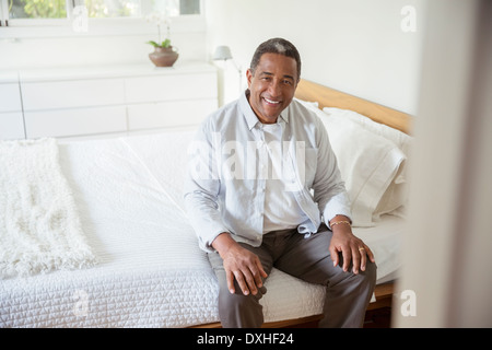 Portrait of smiling senior man sitting on bed Stock Photo