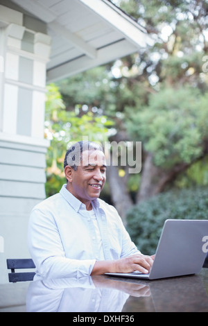 Senior man using laptop at patio table Stock Photo