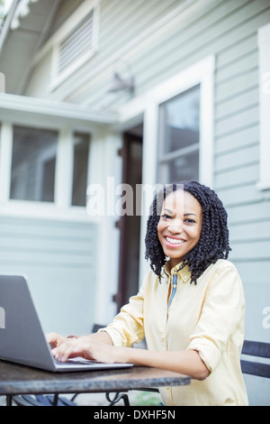 Portrait of smiling woman using laptop at patio table Stock Photo