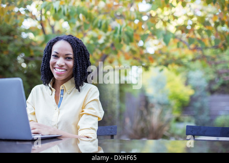 Portrait of smiling woman using laptop at patio table Stock Photo