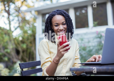 Smiling woman using cell phone and laptop on patio Stock Photo