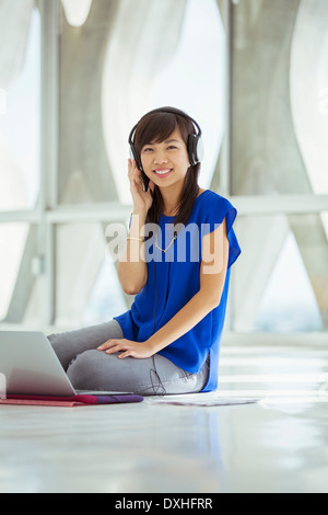 Portrait of casual businesswoman using laptop and wearing headphones on floor Stock Photo