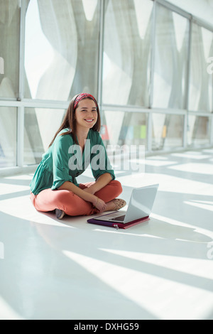 Portrait of confident casual businesswoman using laptop on floor in sunny office Stock Photo