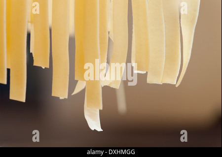 Fresh handmade Italian pasta hanging off a rack before cooking Stock Photo