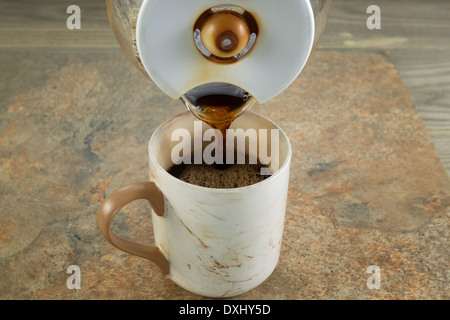 Horizontal photo of freshly brewed black coffee being poured from pot into a ceramic cup of with stone and wood underneath Stock Photo