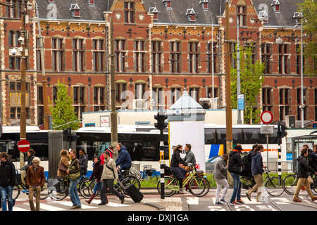 Pedestrians walking over a pedestrian crossing on Damrak in Amsterdam. The Centraal railway station is in the background. Stock Photo