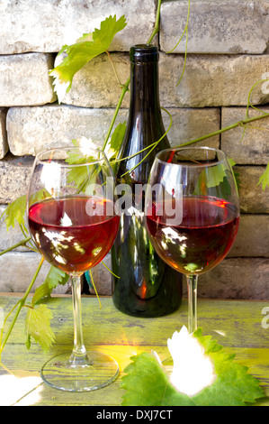Two glasses of red wine on the background of an old brick wall and grape vines. Behind a bottle of wine. Stock Photo