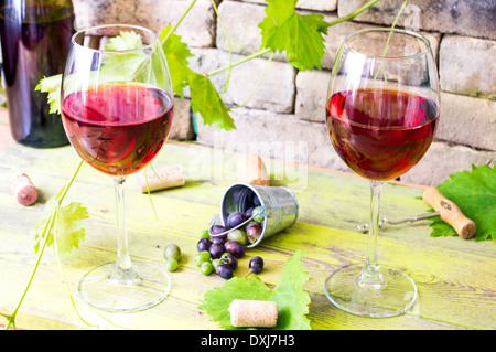 Two glasses of red wine on the background of an old brick wall and grape vines. Behind to a bucket of grape berries Stock Photo
