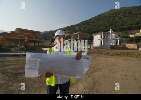Male engineer wearing hard hat looking at plans on building site Stock Photo