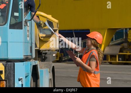 Woman wearing hard hat handing document to man in lorry smiling Stock Photo