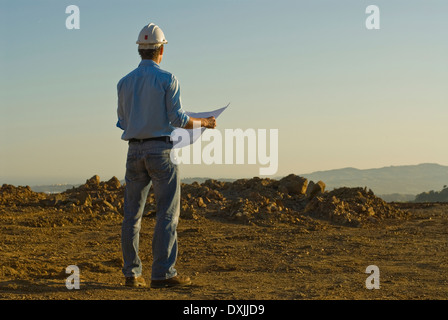 Young engineer with plan on construction site rear view Stock Photo